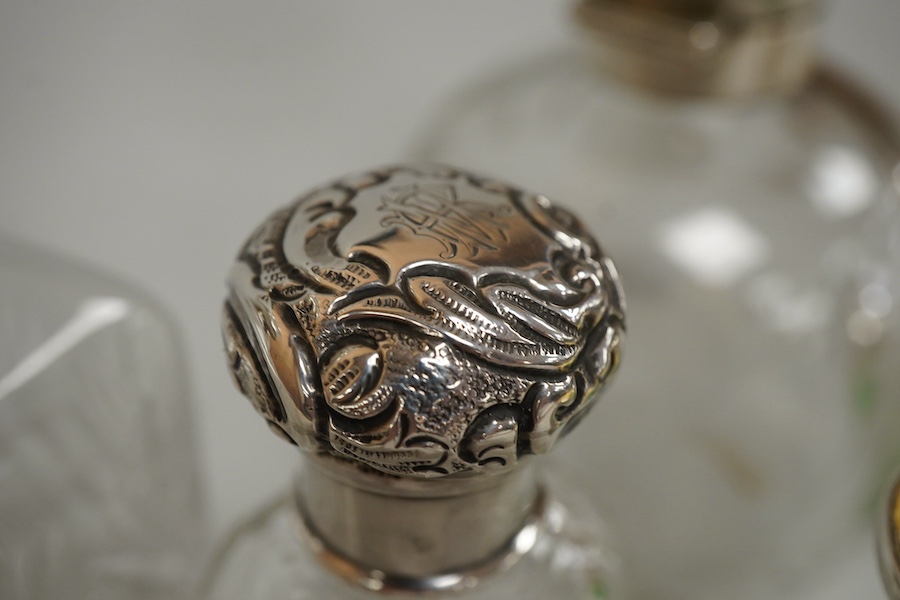 A collection of five silver mounted glass scent bottles to include one with guilloche enamel inset top, a Victorian example hallmarked for Chester 1897 and a cut glass example with mother of pearl top, London 1922, large